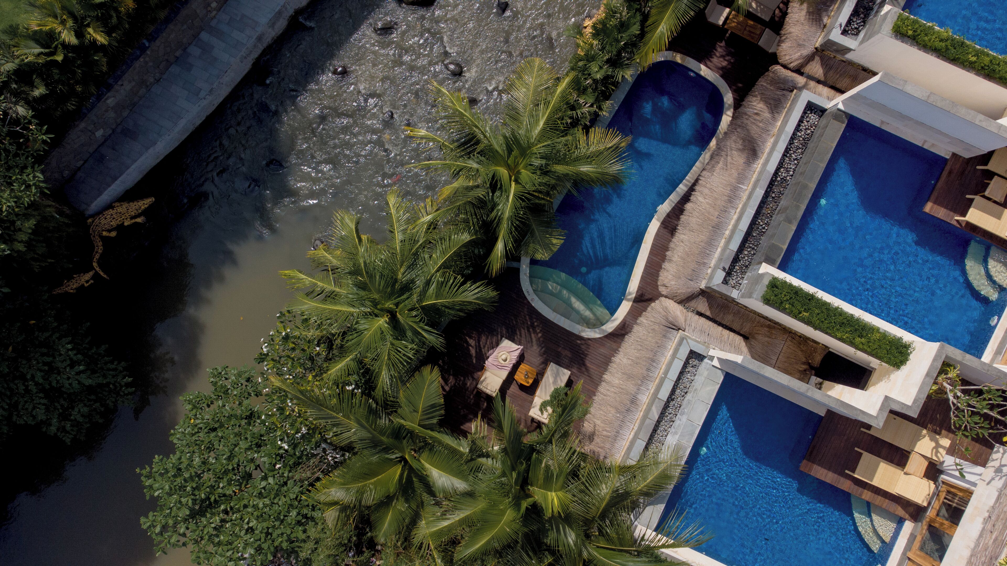 A resort with multiple swimming pools, a river, and lush greenery.
