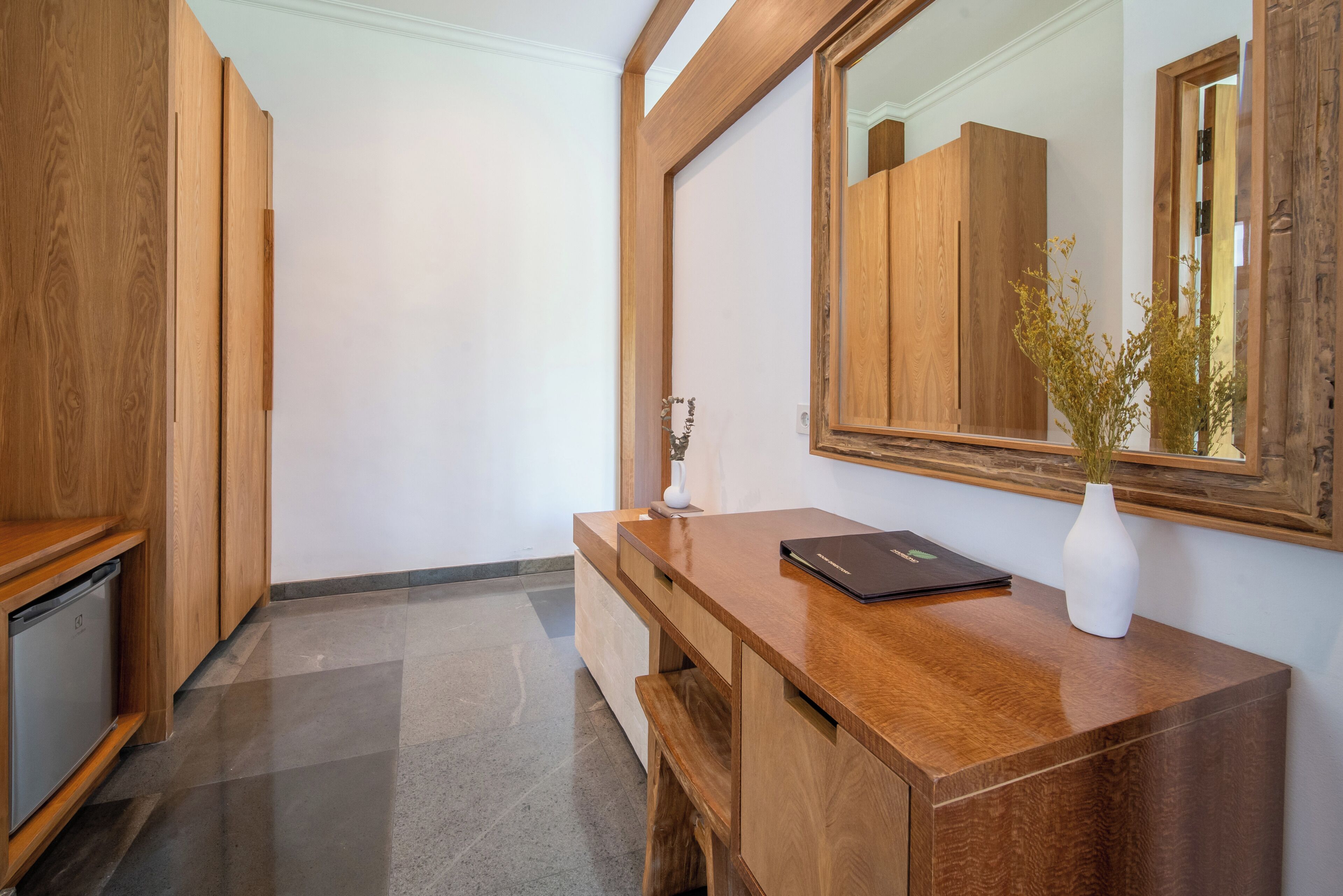 Un bureau en bois avec un miroir, un vase et un ordinateur portable.