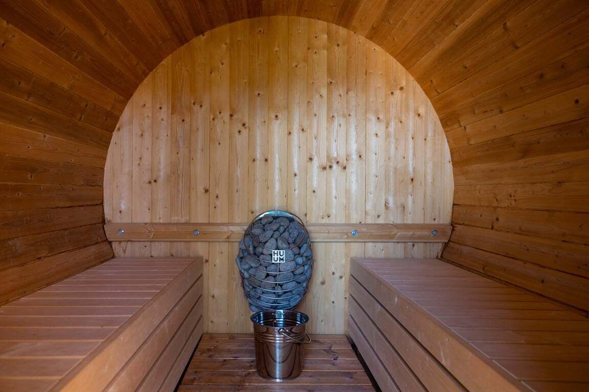 A sauna with a wooden interior, a central bench, and a metal bucket.