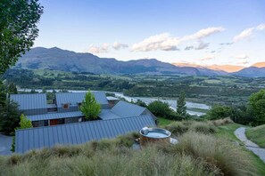 Un bâtiment moderne avec un toit en métal, entouré de pelouse et d’arbres, qui offre une vue sur une vallée et des montagnes.