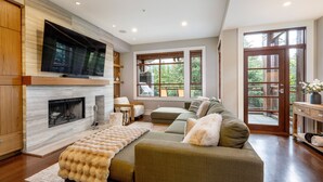 Ein Wohnzimmer mit Kamin, einer Couch, einem Fernseher und großen Fenstern.