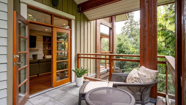 Ein Balkon mit Rattanmöbeln, einem Blumentopf und einer Schiebetür zu einem Innenraum.