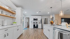 Una cocina moderna con armarios blancos, repisas de madera, electrodomésticos de acero inoxidable e iluminación colgante.