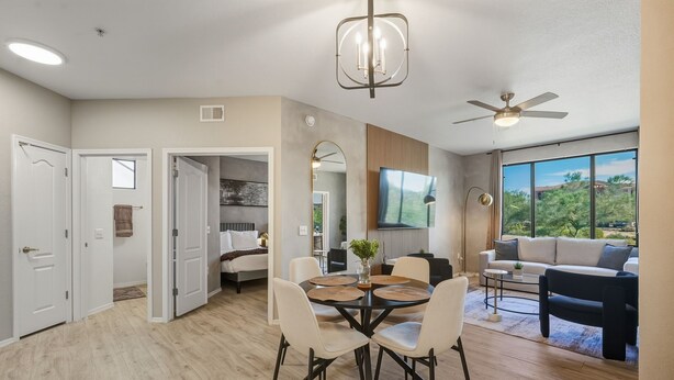 A spacious living area with a dining table, chairs, a sofa, and a TV mounted on the wall. - Modern 2BR/2BA Retreat • Pool • Gym • Free Parking (Phoenix)