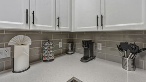 A kitchen with white cabinets, a paper towel dispenser, a coffee maker, a mug rack, and a utensil holder. - Modern 2BR/2BA Retreat • Pool • Gym • Free Parking (Phoenix)
