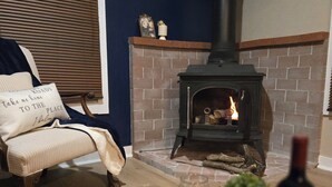 A cozy living room with a brick fireplace, a comfortable chair, and a tray with glasses and a bottle. - Cozy Winter Cabin • Wood Stove • Mountain View (Chesterville)
