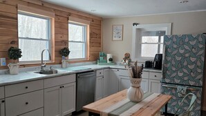 A kitchen with wooden cabinets, a sink, a dining table with chairs, and a refrigerator. - Cozy Winter Cabin • Wood Stove • Mountain View (Chesterville)