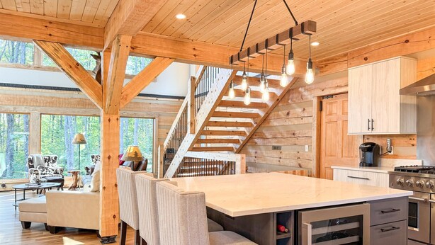 Una cocina amplia con una isla central, vigas de madera y una escalera que sube a un nivel superior.