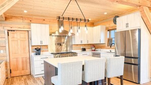 Una cocina moderna con armarios de madera, una isla central con taburetes de bar, electrodomésticos de acero inoxidable e iluminación colgante.