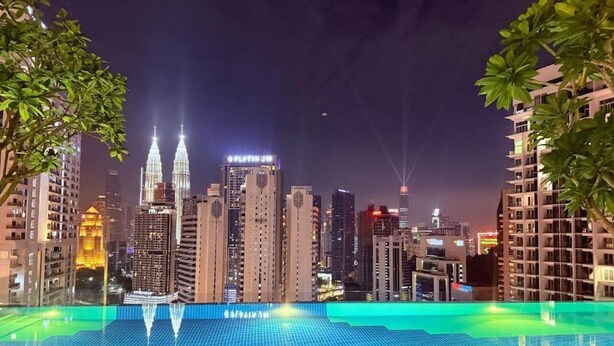 Una piscina en la azotea con vistas a la ciudad, incluyendo las Torres Petronas, rodeada de edificios.