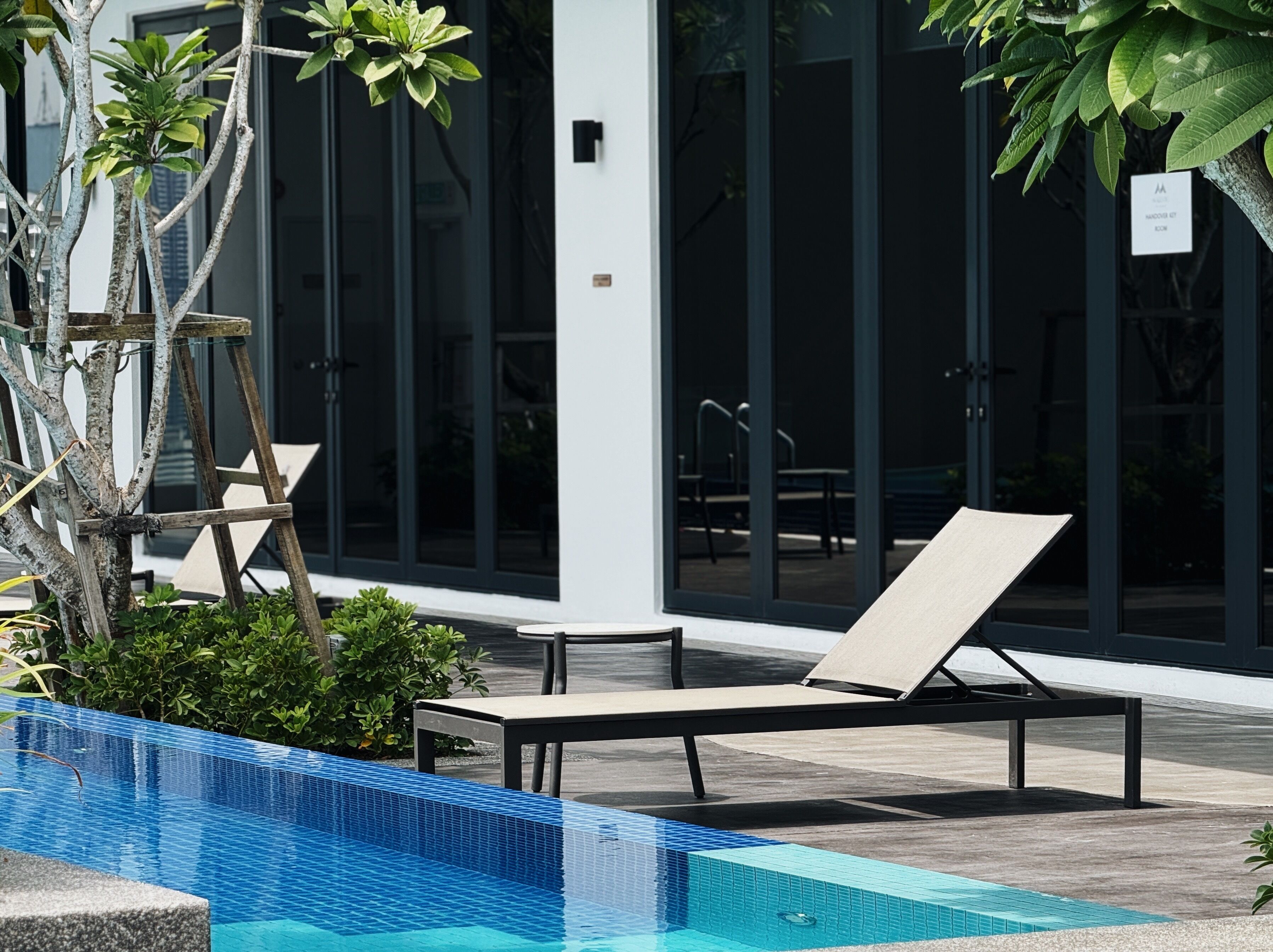 A poolside area with a lounge chair, a small pool, and a modern building with large windows in the background.