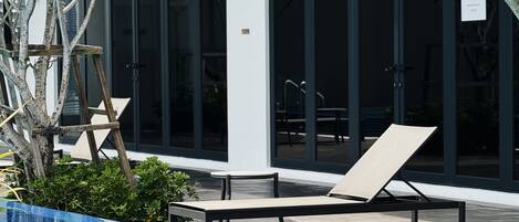 A poolside area with a lounge chair, a small pool, and a modern building with large windows in the background.