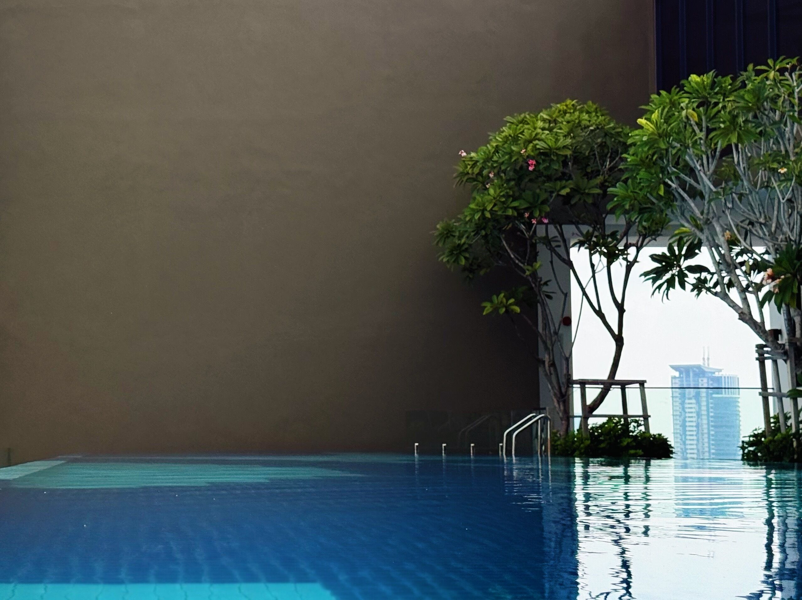 An indoor swimming pool with clear water, surrounded by greenery and a high-rise building in the background.