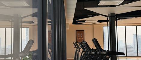 A gym with exercise equipment and large windows offering city views.