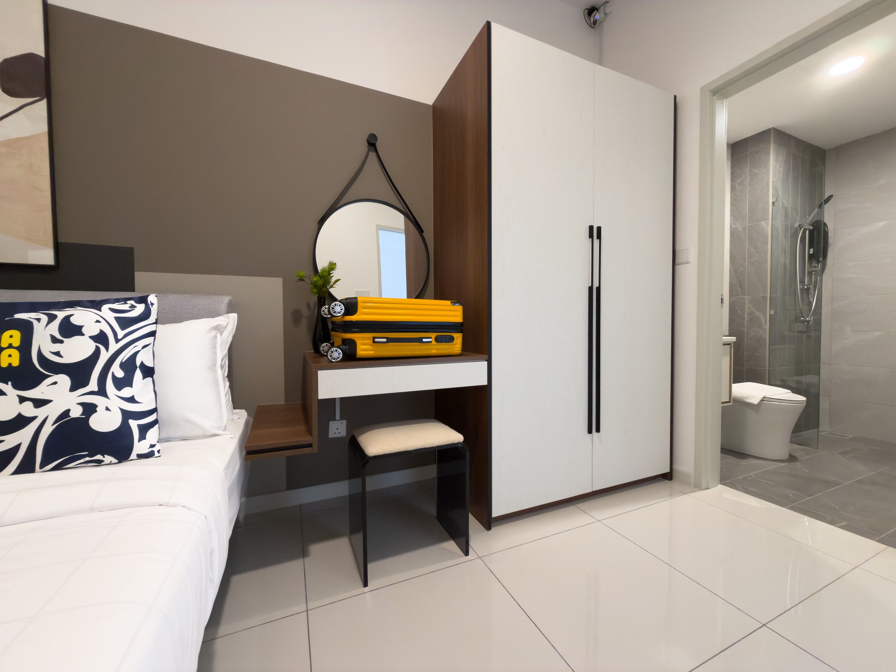 Una habitación de hotel moderna con cama, escritorio con espejo, armario y zona de ducha.