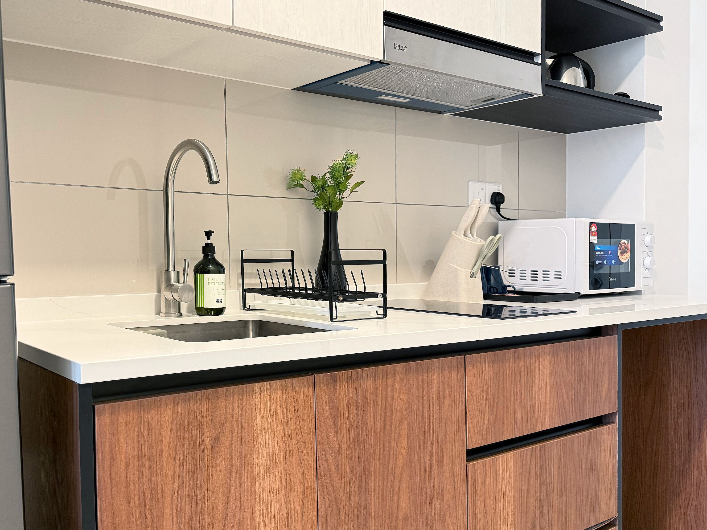 Una cocina moderna con un lavamanos de acero inoxidable, un escurreplatos, una planta en maceta y un microondas.