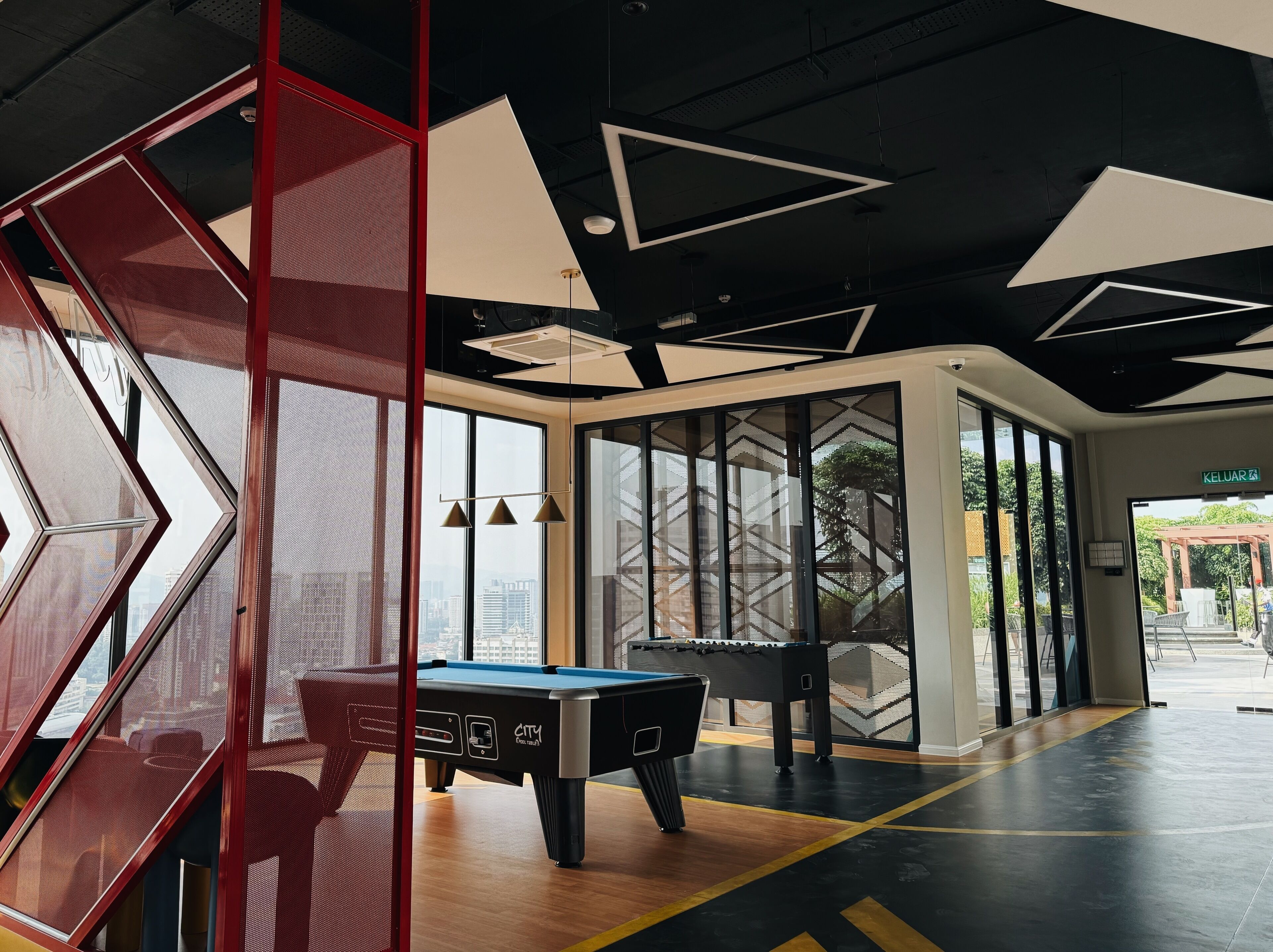 A pool table in a modern indoor space with geometric ceiling designs and large windows.