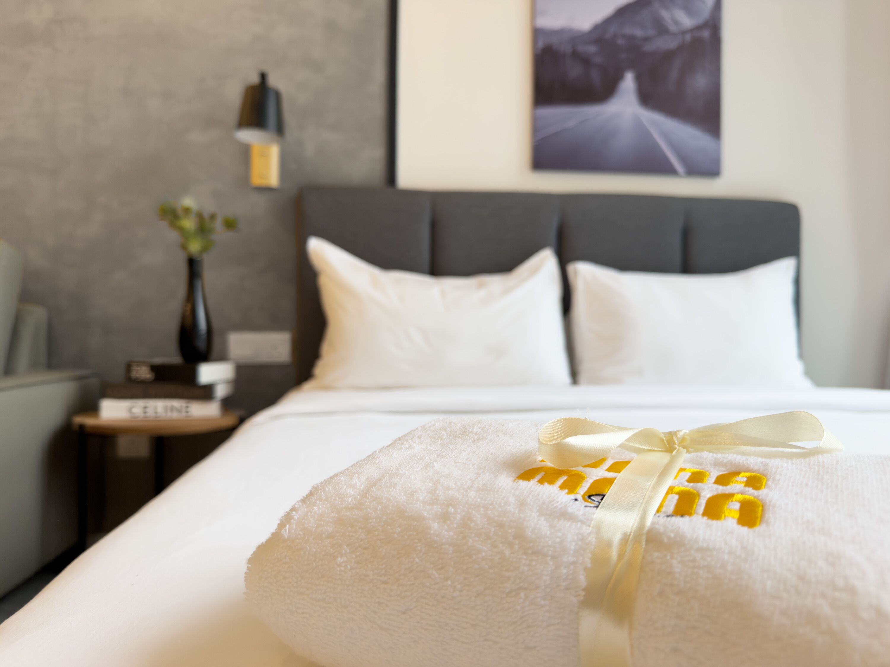 A neatly made bed with white linens and a towel with a yellow ribbon.