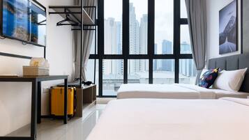 A modern hotel room with a large window, a bed, a desk with a suitcase, and a coat rack.