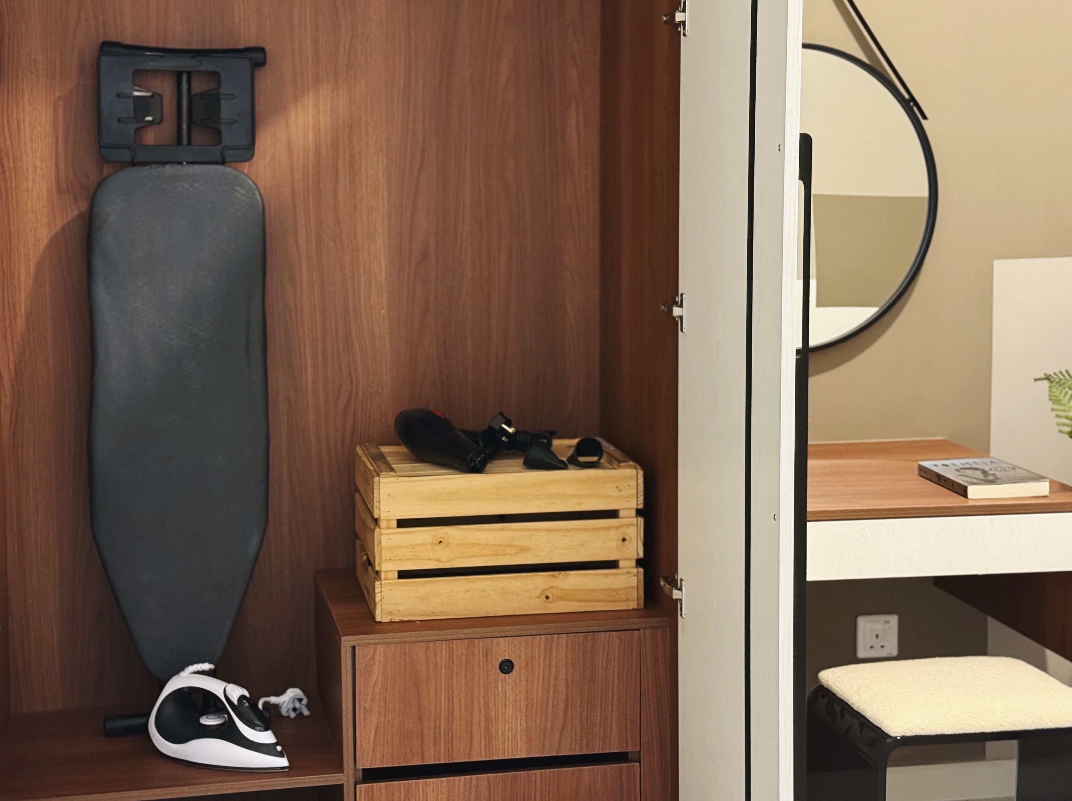 A wooden wardrobe with a mirror, a pair of shoes, and a book on a wooden shelf.