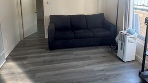 A room with a dark-colored sofa, a standing fan, and a window with curtains. - Cozy 1-bedroom house in cool Long Beach with AC (Long Beach)