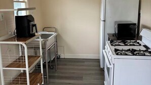A compact kitchen with a white stove, a microwave, and a coffee maker on a cart. - Cozy 1-bedroom house in cool Long Beach with AC (Long Beach)