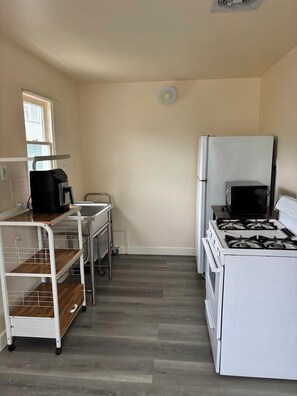 A compact kitchen with a white stove, a microwave, and a coffee maker on a cart. - Cozy 1-bedroom house in cool Long Beach with AC (Long Beach)