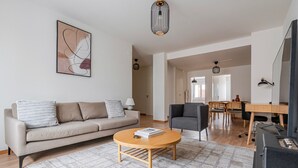 Ein modernes Wohnzimmer mit einer Couch, einem runden Couchtisch, einem grauen Sessel und einem Essbereich mit einem Holztisch und Stühlen.