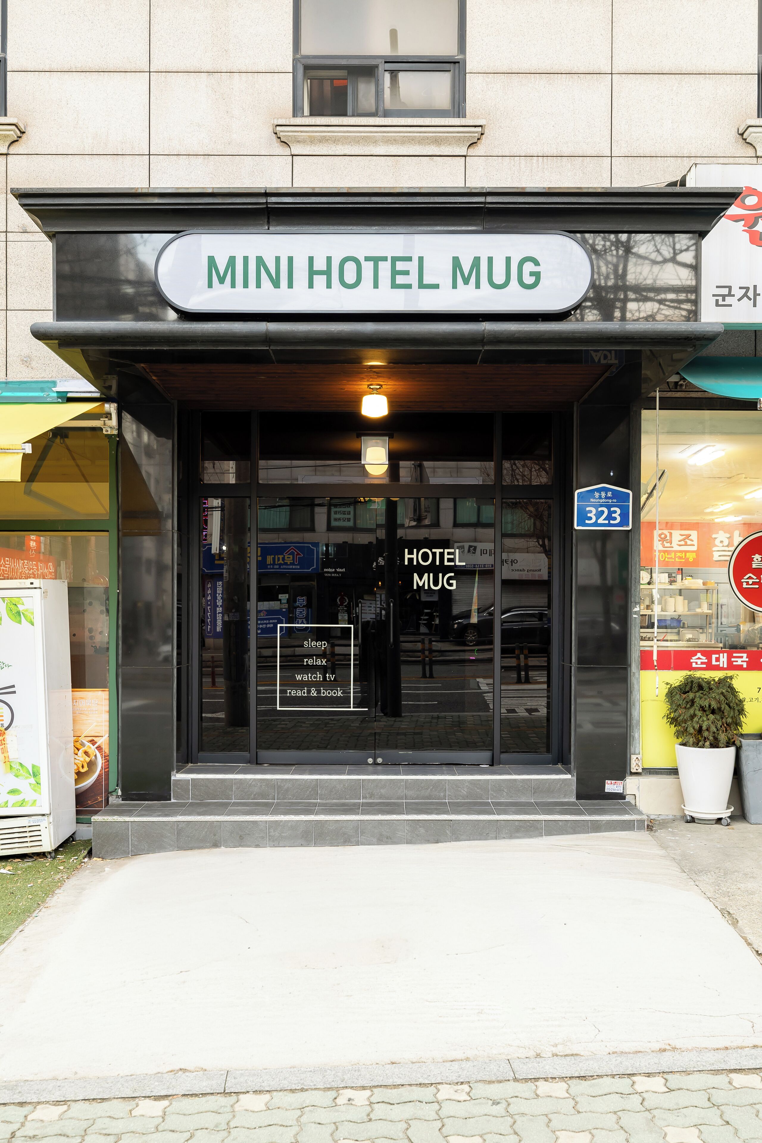 The entrance to a hotel named "MINI HOTEL MUG" with a sign indicating the address as 323.