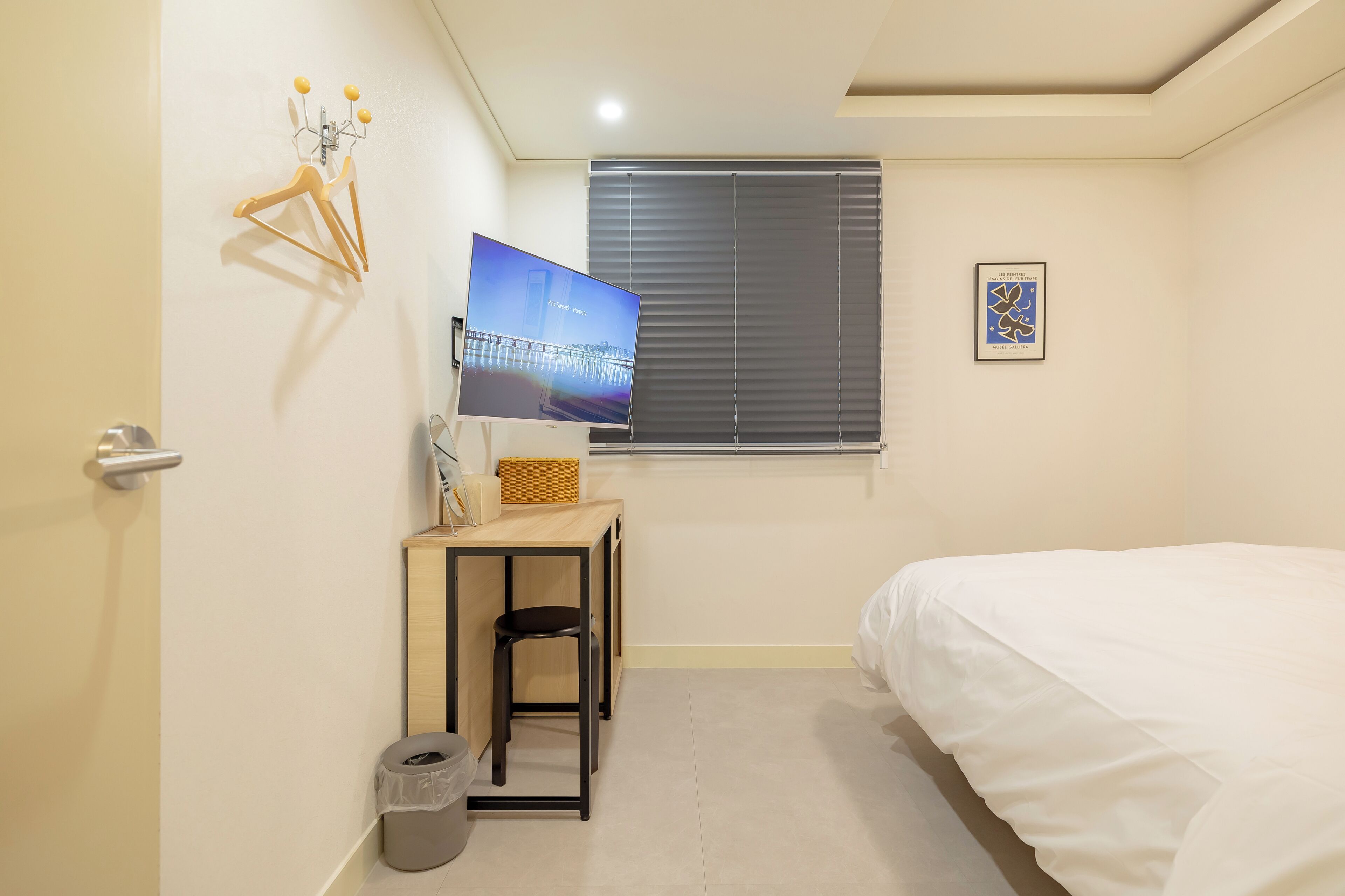 A small, neatly arranged bedroom with a bed, a desk, a chair, and a television.