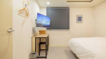 A small, neatly arranged bedroom with a bed, a desk, a chair, and a television.