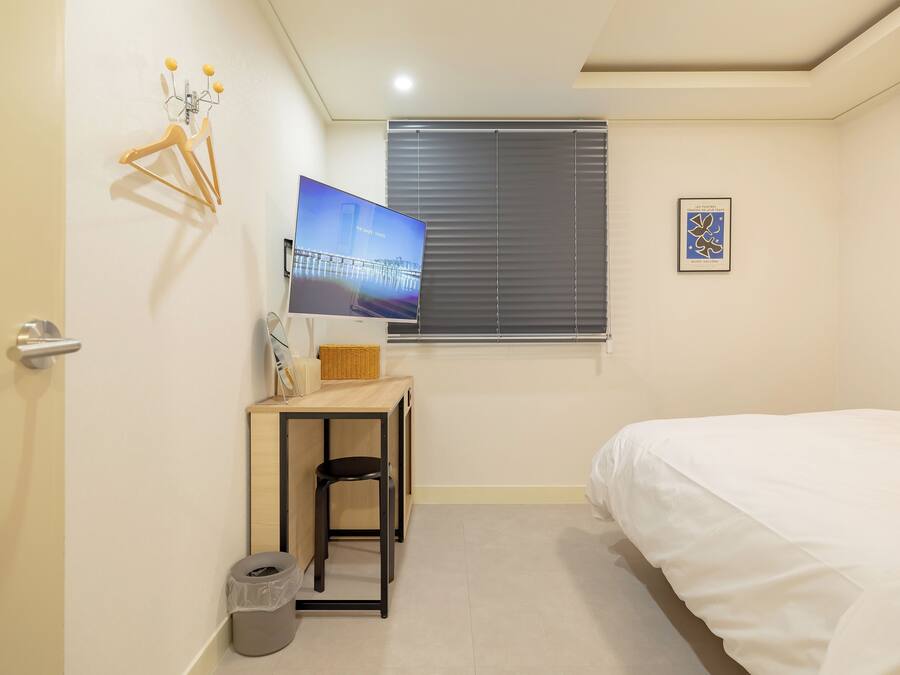 A small, neatly arranged bedroom with a bed, a desk, a chair, and a television.