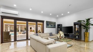 A spacious living room with a beige sectional sofa, a flat-screen TV, and a large potted plant. - Stunning Luxury Pool OasisRooftop W/ Ocean Views (Noord)