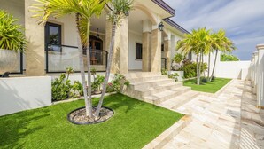 A well-maintained outdoor area with a stone pathway leading to a set of stairs, surrounded by palm trees and a neatly trimmed lawn. - Stunning Luxury Pool OasisRooftop W/ Ocean Views (Noord)