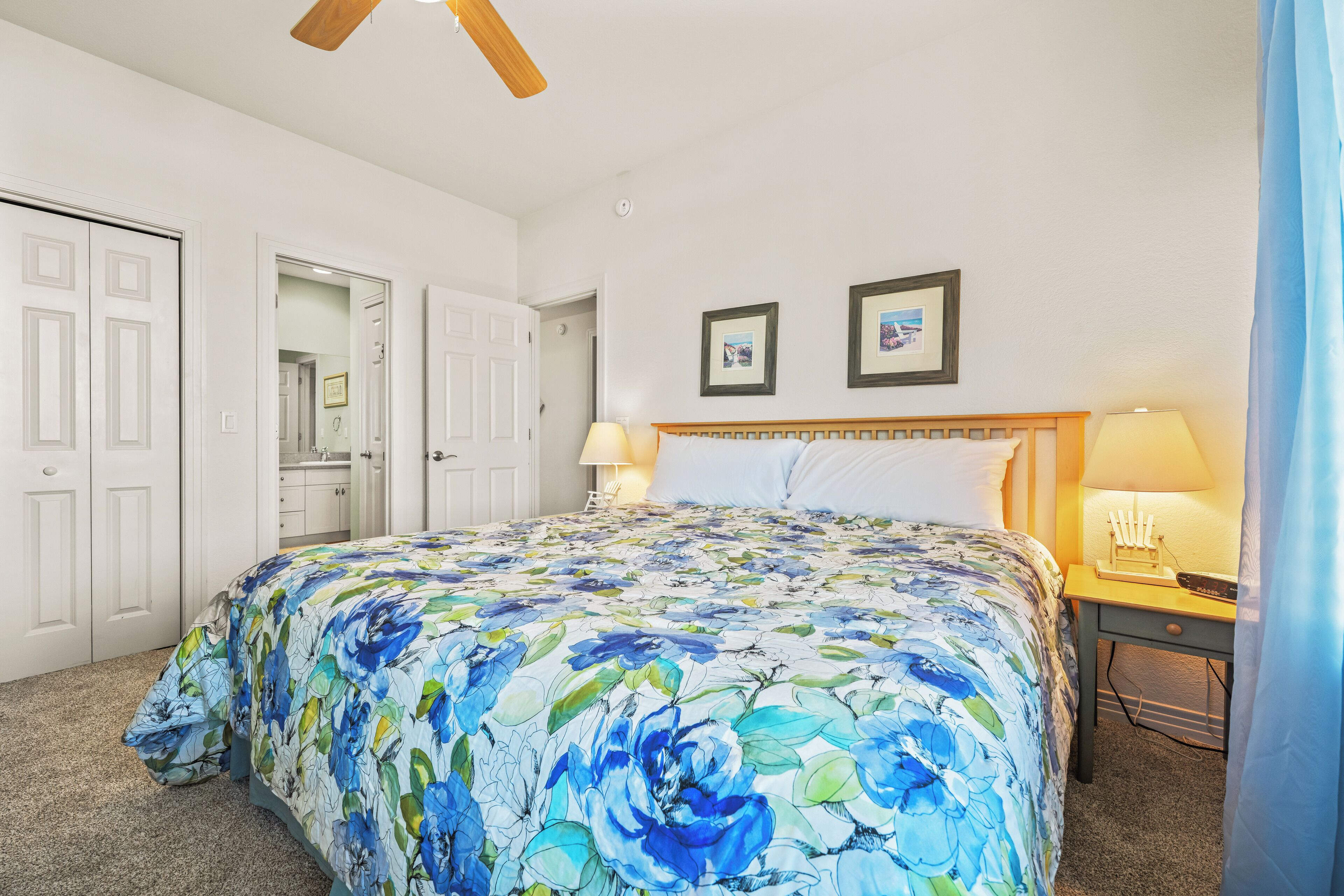 A bedroom with a floral bedspread, two bedside lamps, a wooden headboard, and a door leading to a bathroom.