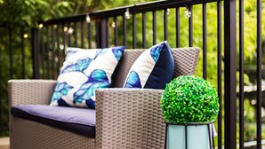 A wicker sofa with blue and white patterned cushions, a small potted plant, and a black metal railing. - Bright 6 BD Executive Home - 2 Kitchens - Garage - NFLX (Edmonton)