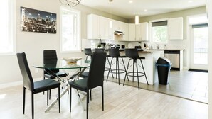 A modern kitchen with white cabinets, a glass dining table, and black chairs. - Bright 6 BD Executive Home - 2 Kitchens - Garage - NFLX (Edmonton)