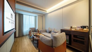 A modern hotel room with a sofa, a coffee table, a TV, and a minibar. - Kaiyuan Mingting Hotel (Chengdu)