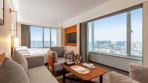A modern hotel room with a large bed, a sofa, a dining table, and a city view through large windows. - Kaiyuan Mingting Hotel (Chengdu)