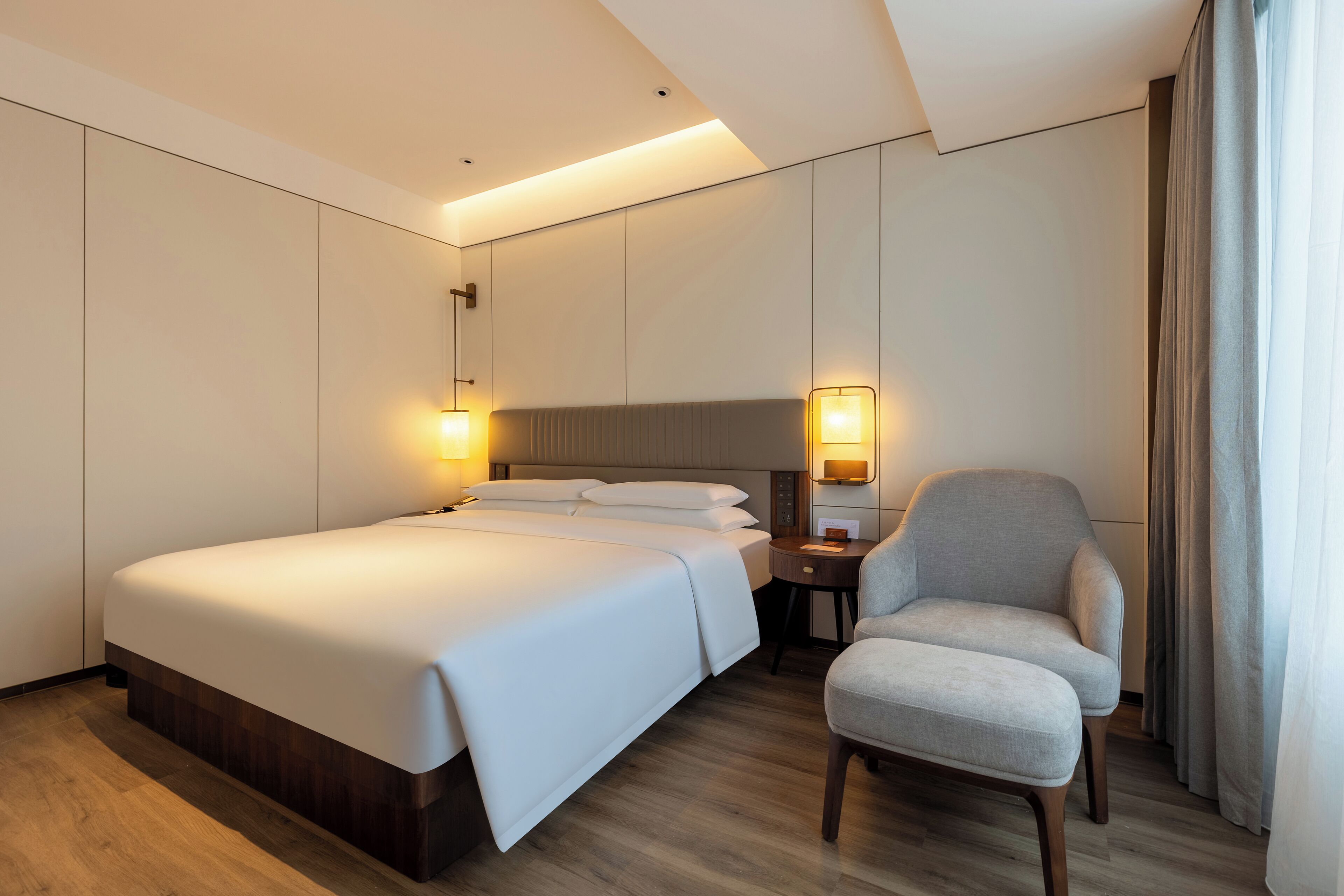 Una habitación de hotel con una cama grande, mesitas de noche, una silla y una mesita auxiliar.