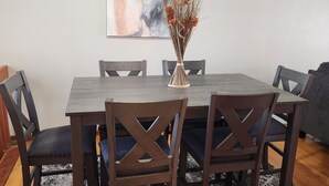 A dining area with a rectangular table, six wooden chairs, a vase with dried flowers, and a large abstract painting on the wall. - The Cozy Retreat 1.7 miles from the Naval base (North Chicago)