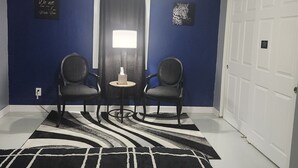 A room with blue walls, two chairs, a table, a black and white rug, a ceiling light, and a door. - The Cozy Retreat 1.7 miles from the Naval base (North Chicago)
