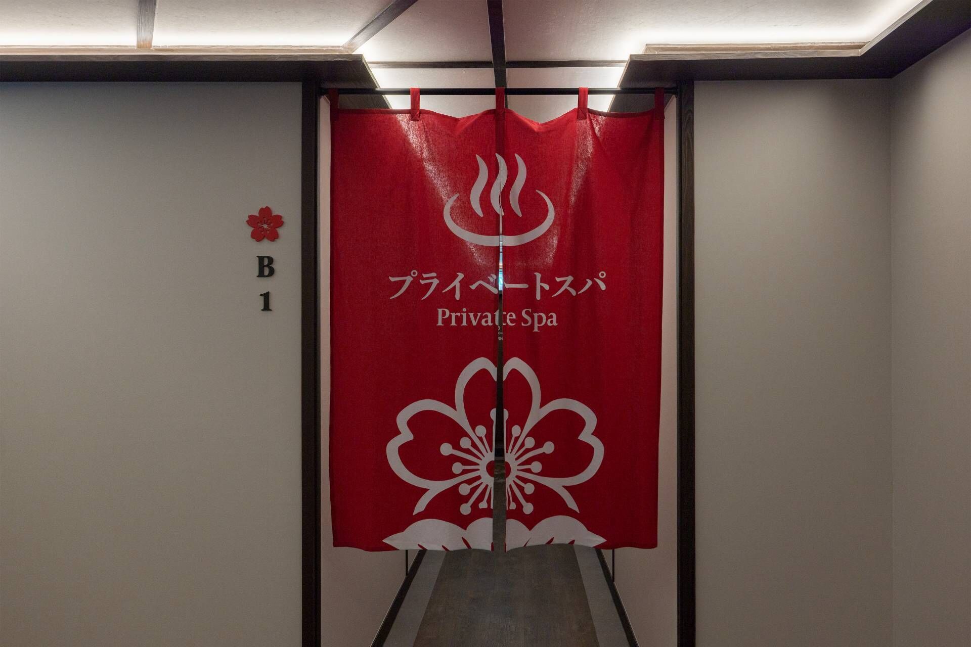 A red banner with Japanese text and a white flower design, hanging in a hallway with a sign indicating room B1.