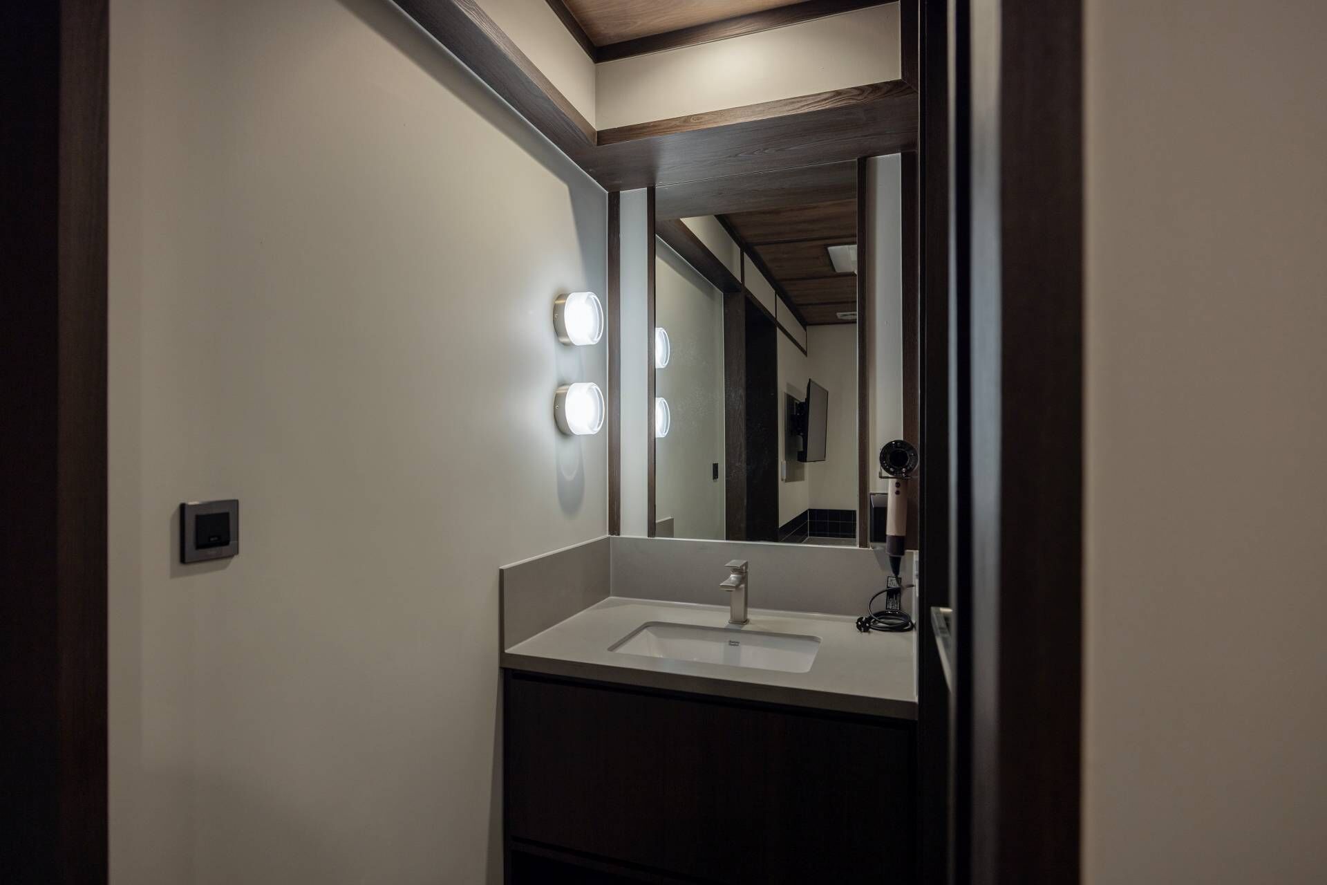 Un baño con un lavamanos blanco, un espejo y tres luces fijadas en la pared.