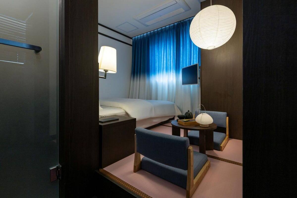 Une chambre d’hôtel avec un lit, un bureau avec une lampe, une chaise et une table avec une lampe.