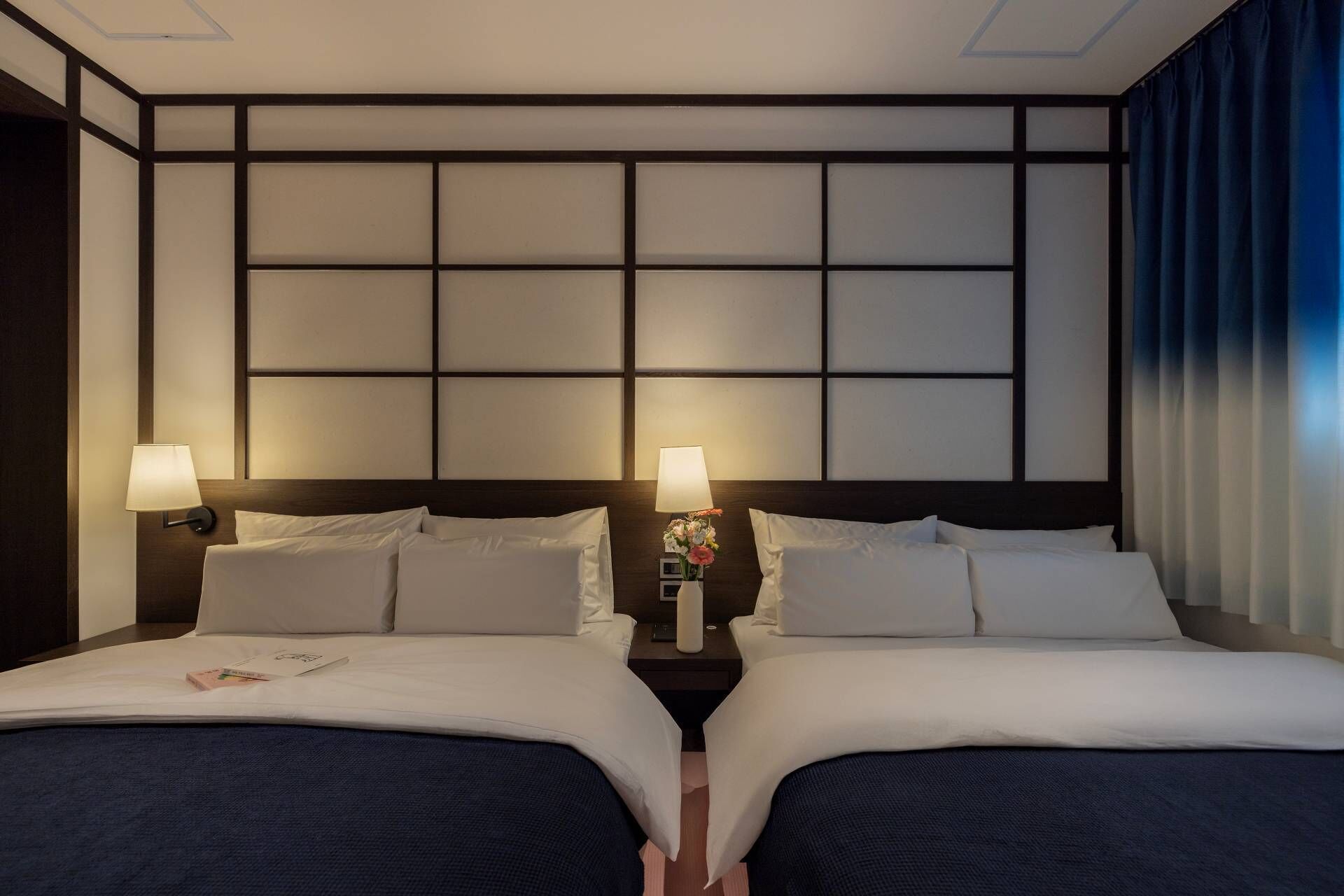 Une chambre d’hôtel avec deux lits, une table de chevet avec une lampe et un vase décoratif.