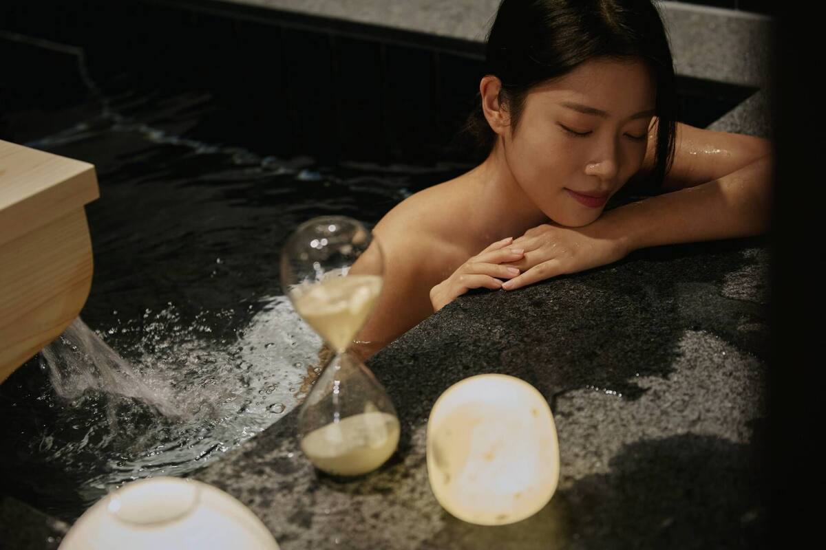 Une personne dans un bain à remous, avec un sablier et une pierre.