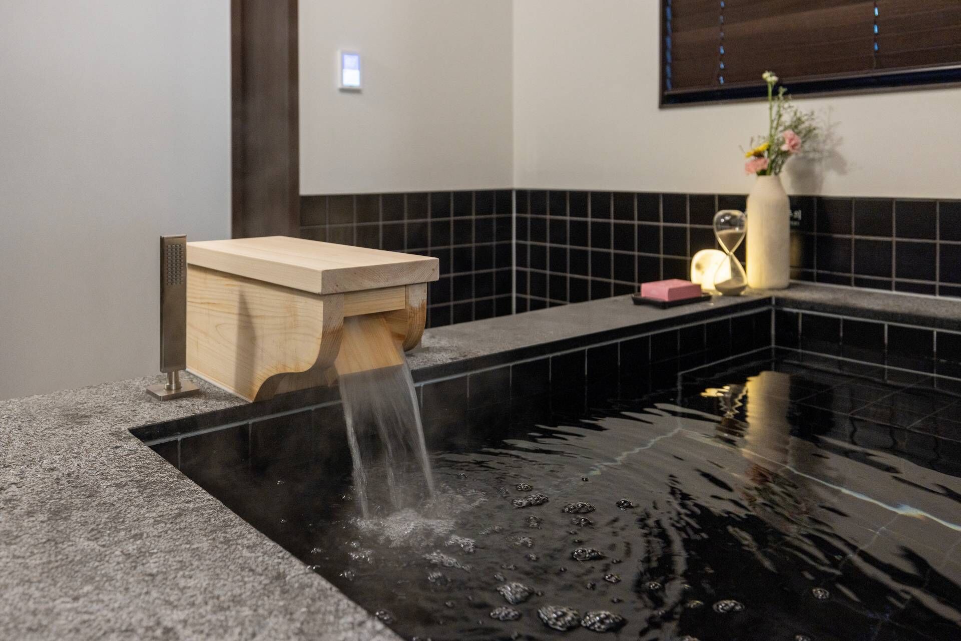 A modern bathroom with a wooden washbasin and a black tiled wall.