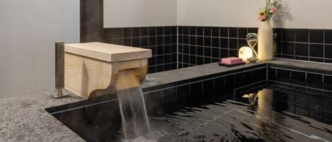 A modern bathroom with a wooden washbasin and a black tiled wall.