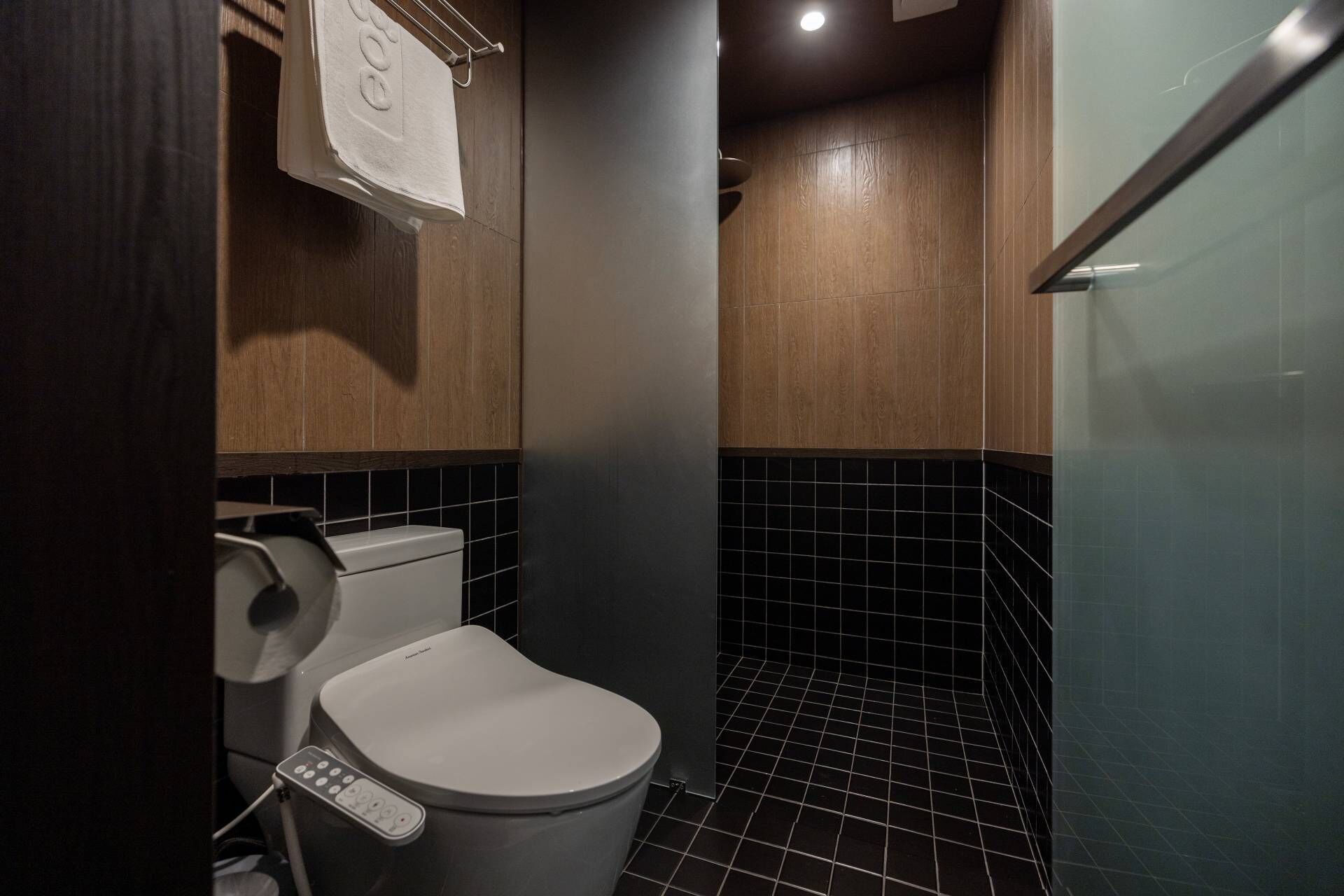 A modern bathroom with a toilet, a hand dryer, and a control panel.